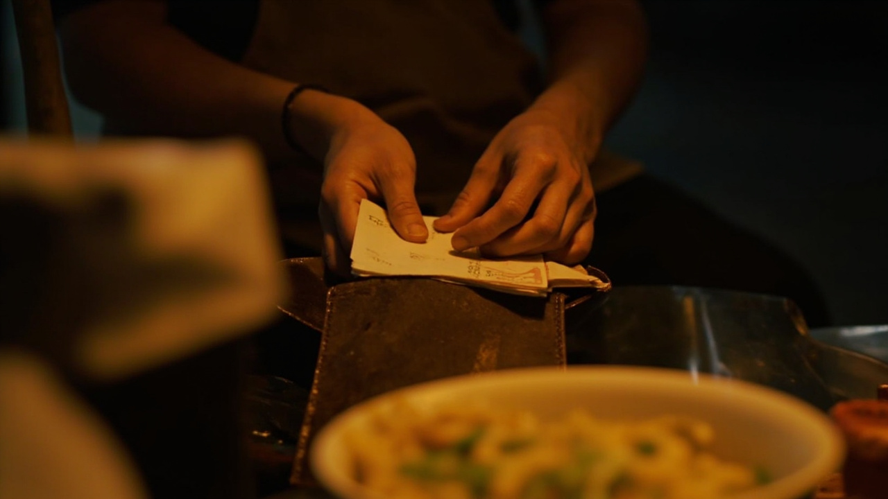 Hands tucking cash into a billfold at a night market